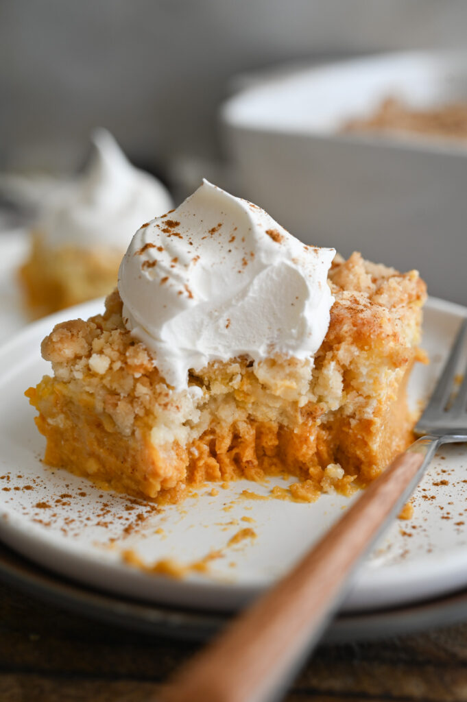 A piece of pumpkin dump cake on a white plate with a fork that has taken a bite out of the dessert.