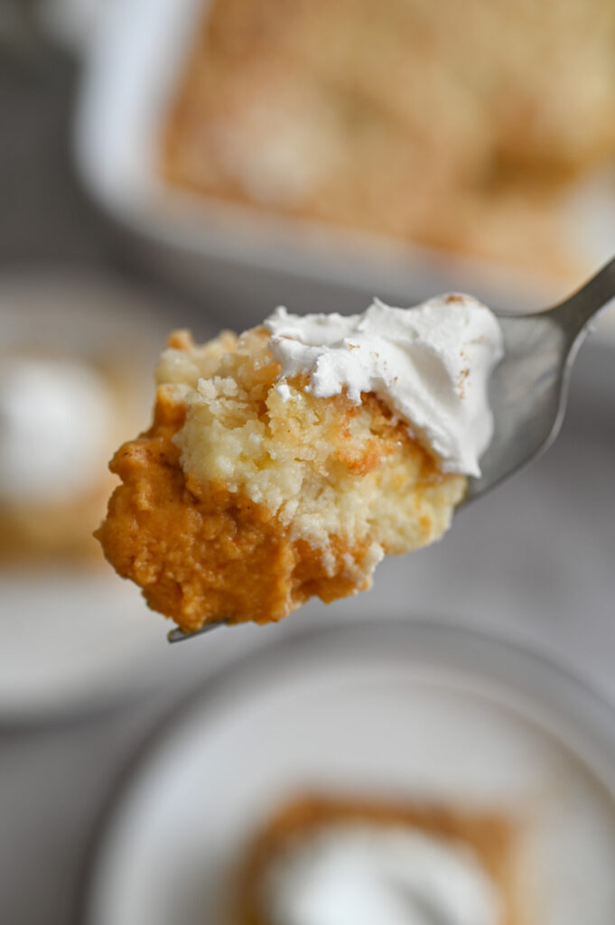 A forkful of a pumpkin dessert with a cream cheese layer, crumb topping and whipped cream on top.