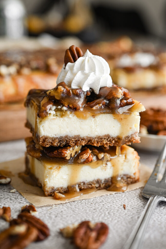 Two pecan pie cheesecake bars stacked on top of eachother and topped with whipped topping.