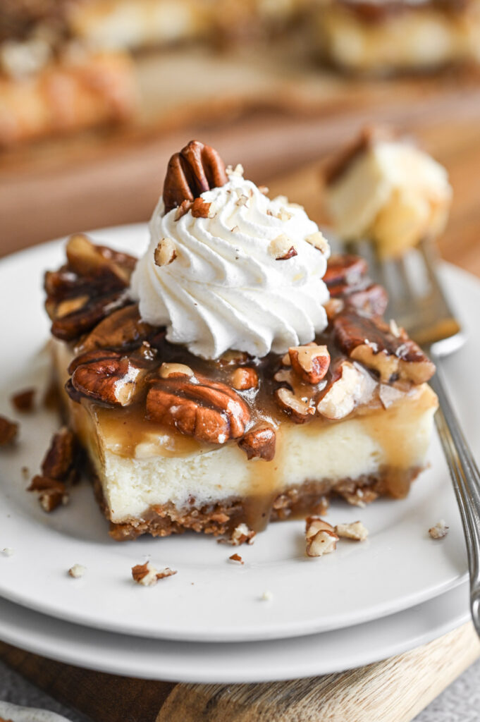 A pecan pie cheesecake square with a dollop of whipped topping and a pecan on top.