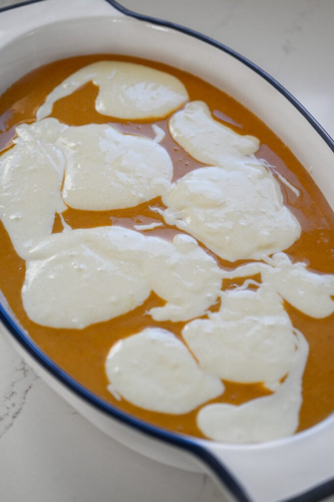 Pumpkin filling in a ceramic dish with spoonfuls of cream cheese filling on top.