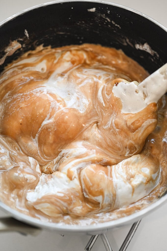 A rubber spatula stirring marshmallow cream and peanut butter into a hot brown mixture.