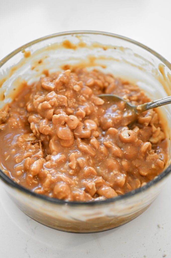 Chopped peanuts stirred into a glass bowl of caramel sauce.