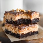 Two Snickers brownies stacked up; the top one has a bite taken out of it.