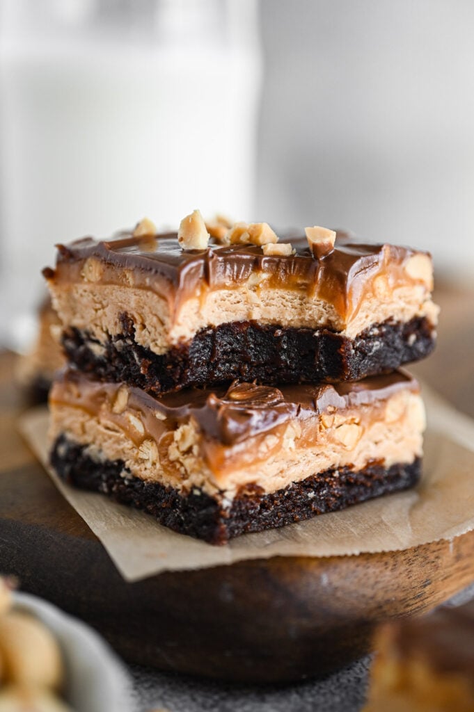Two Snickers brownies stacked up; the top one has a bite taken out of it.