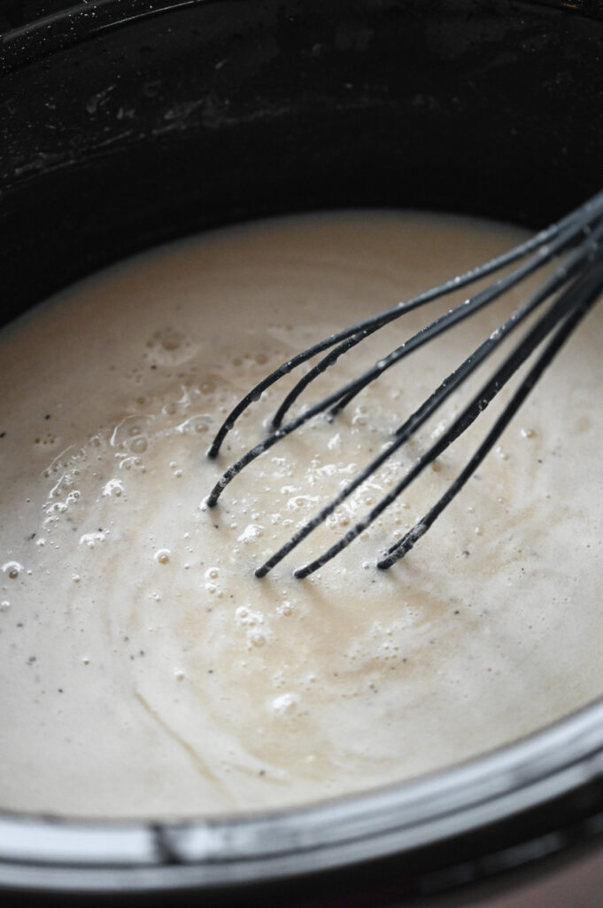 A whisk combining ingredients in a black crock of a slow cooker.