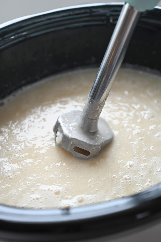 An immersion blender mixing some potatoes to smooth out the soup base.