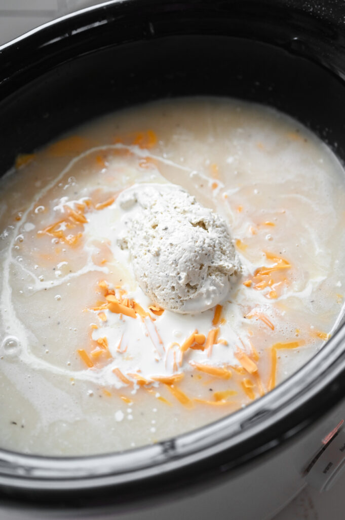 A slow cooker with cream cheese, whipping cream and a yellow cheese added.