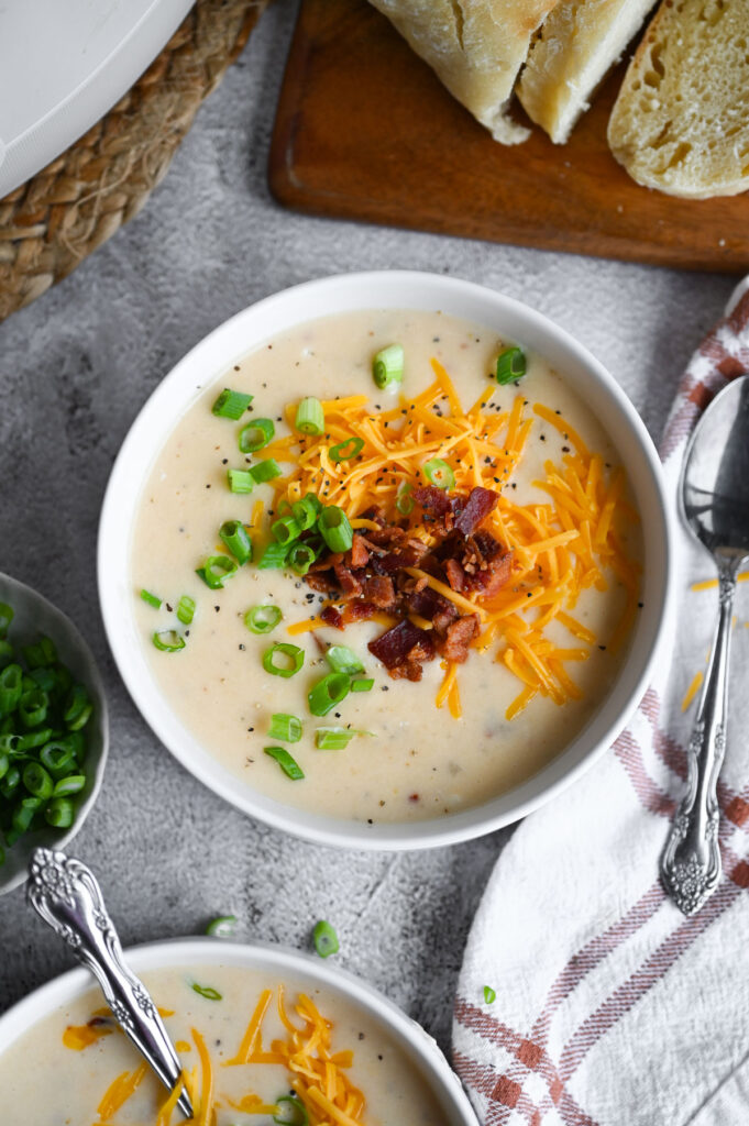 Overhead view of a bowl of a creamy potato soup topped with green onions, black pepper, bacon, and cheddar cheese.