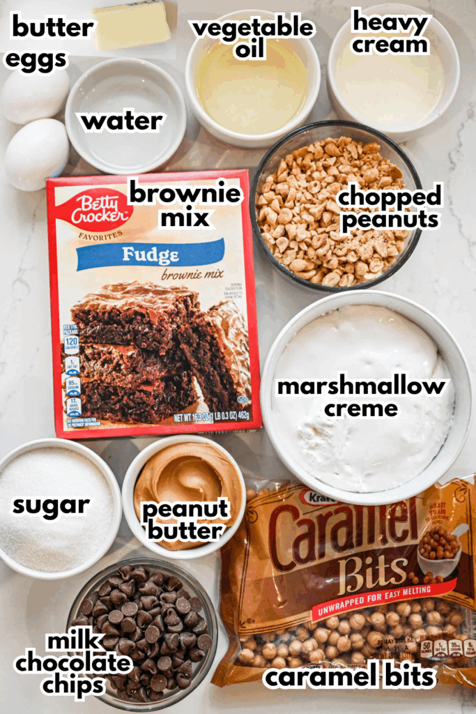 The ingredients needed to make snickers brownies on a white marble background.