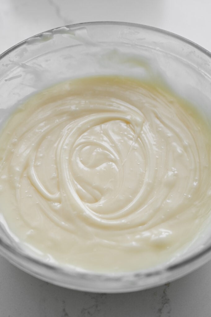 White chocolate ganache melted until smooth in a clear glass bowl.