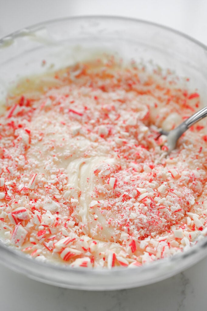 Peppermint candies being stirred into a bowl of melted white chocolate.
