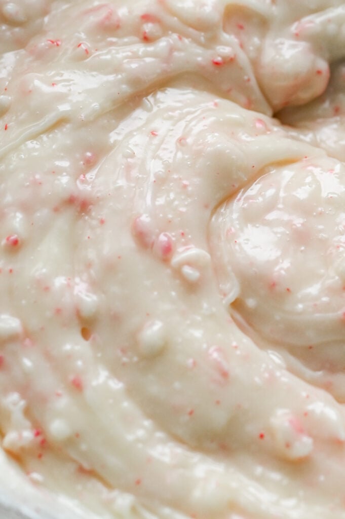Peppermint candies being stirred into a white chocolate mixture.