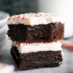 Two peppermint bark brownies stacked on each other; the top one has a bite out of it.
