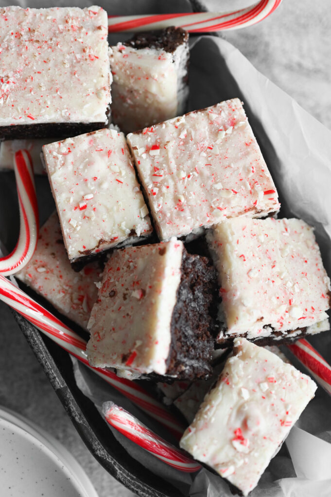 Several peppermint fudge brownies in a metal tray with candy canes around it.