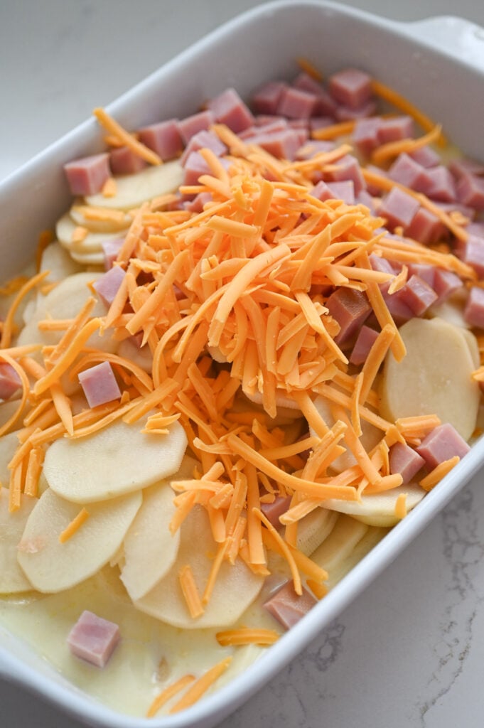 Sliced russet potatoes, cheese and ham in a baking dish.