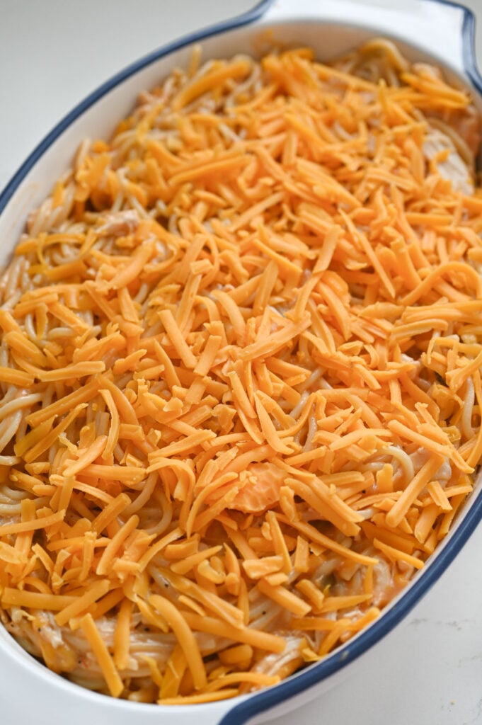 An oval casserole dish with a casserole topped with cheese ready to go into the oven.