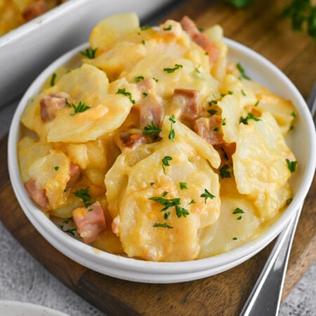 A plate with scalloped potatoes and ham on it and a sprinkle of fresh parsley.