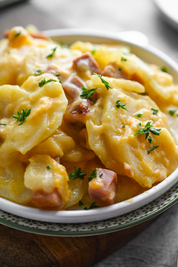 A white plate with a serving of scalloped potatoes and ham on it; sprinkled with fresh parsley.