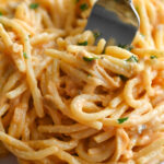 A plate with a light colored spaghetti bake on a white plate with a silver fork twirling a bite.