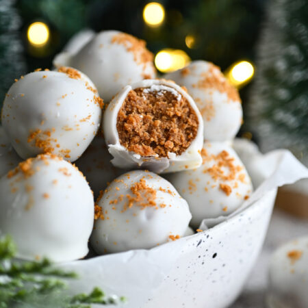A bowl of Biscoff Truffles; one in the middle has a bite out of it showing the brown interior.