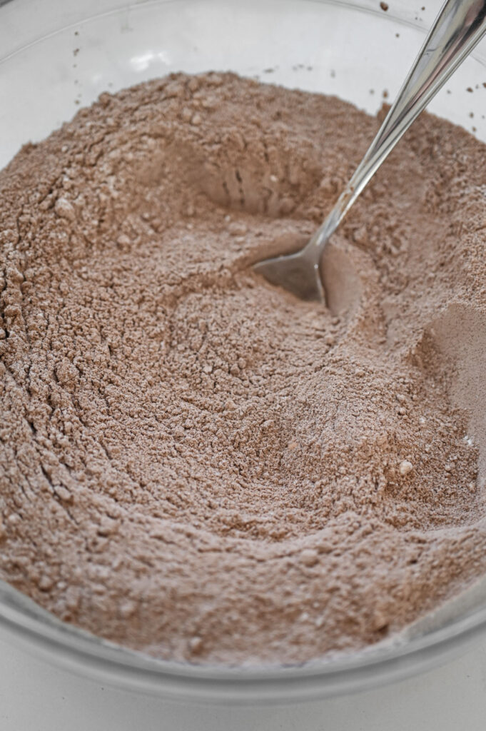 Dry ingredients for a chocolate cake in a clear bowl.