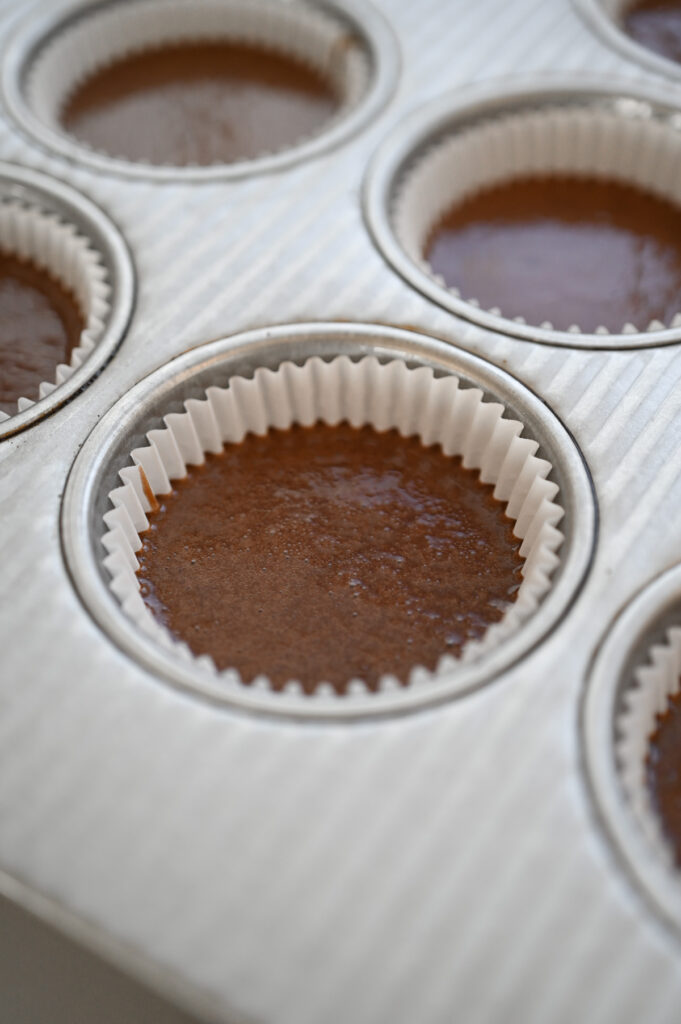 A cupcake pan with liners filled about 2/3 full with chocolate cake batter.