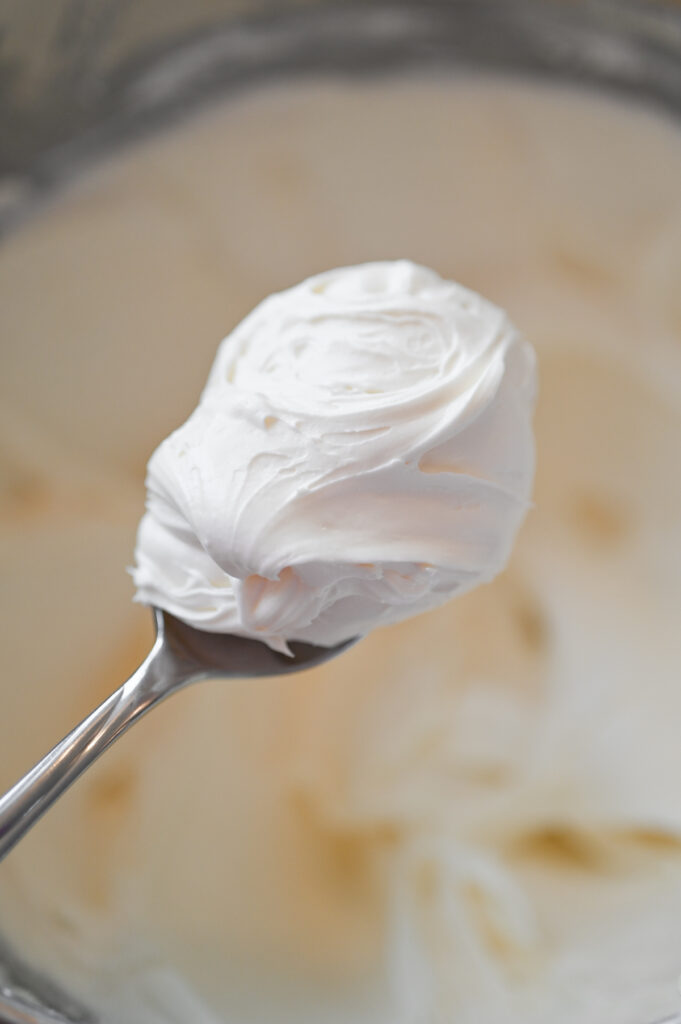 A silver spoon with a scoop of a fluffy white frosting on it.