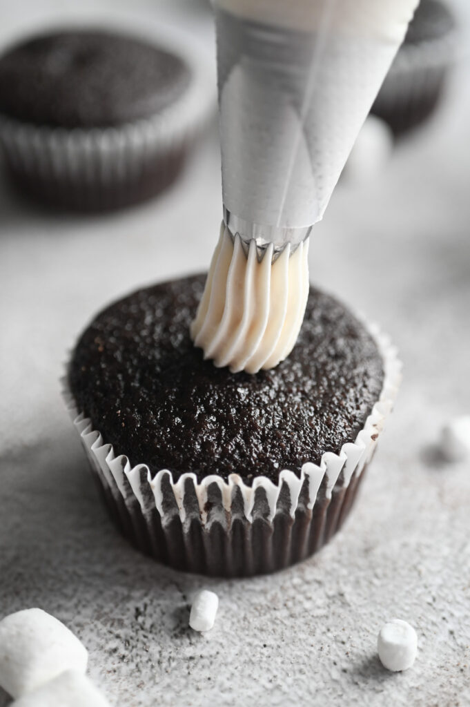 A piping bag being used to put frosting on a chocolate cupcake.