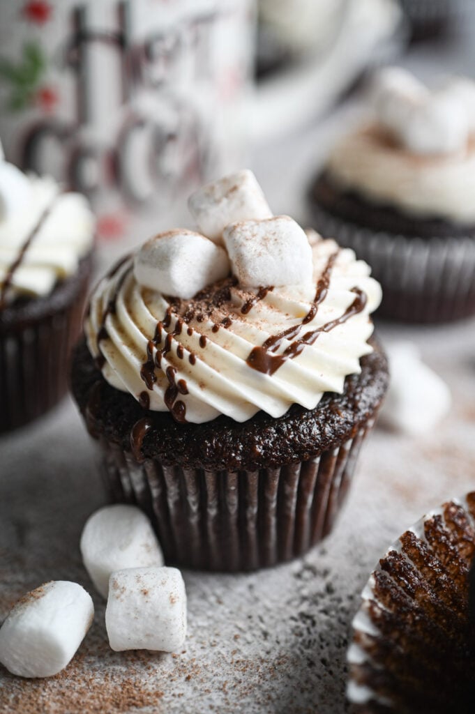 A chocolate cupcake with a white frosting, a chocolate drizzle and marshmallows on top.