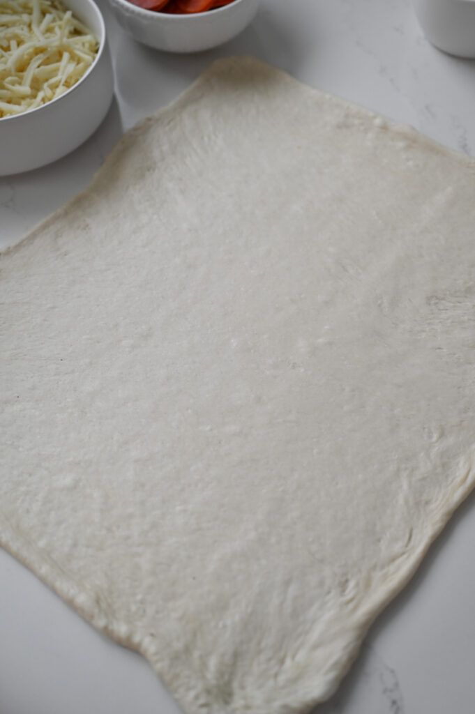 Dough that has been rolled out into a rectangle shape on a white countertop.