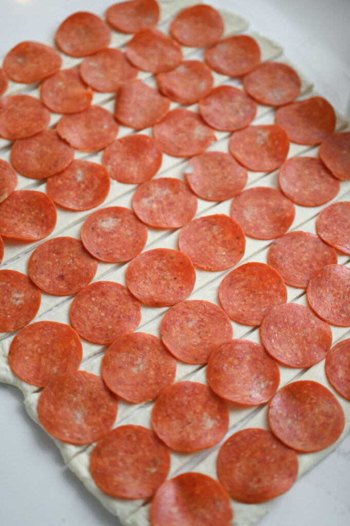 A rectangle of dough cut into 9 strips and topped with pepperoni slices.