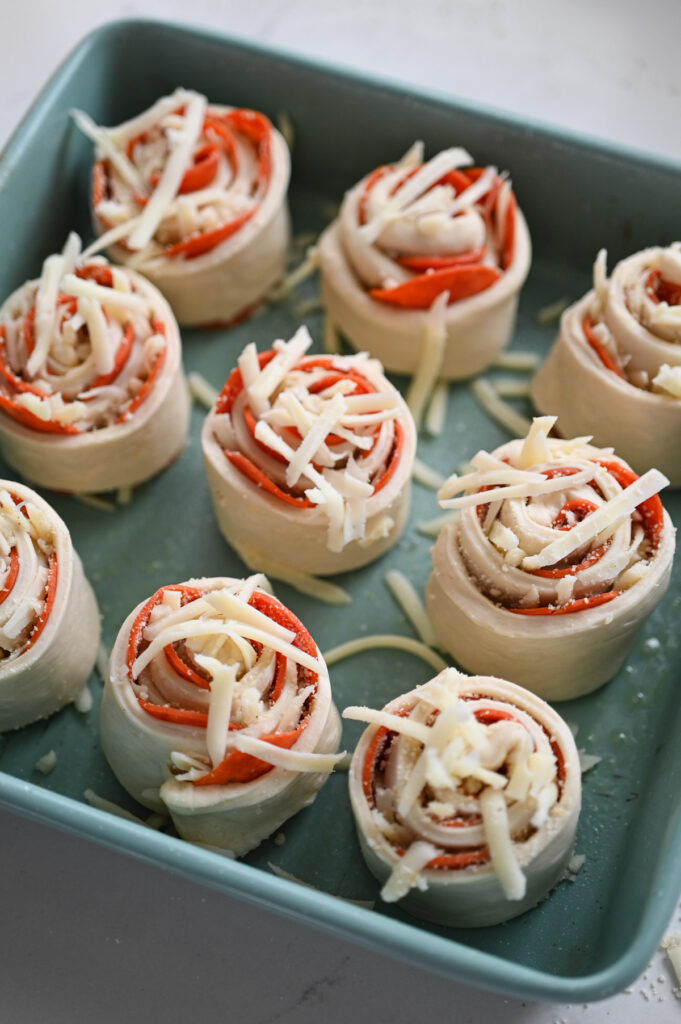 Nine pepperoni pizza rolls in a square teal baking pan.