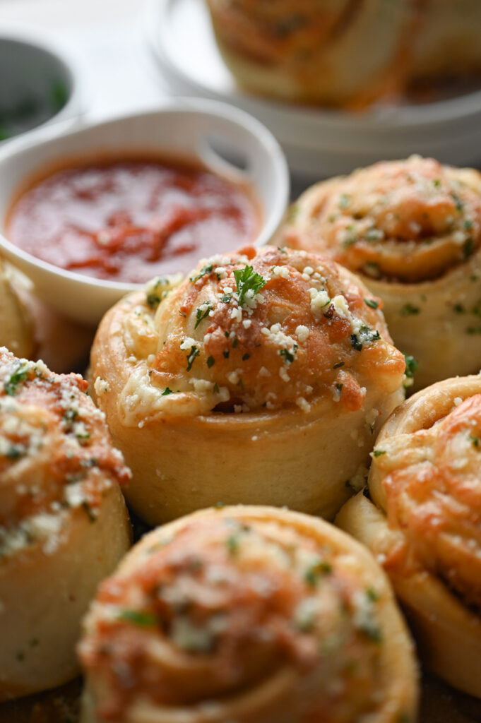 Pepperoni rolls topped with garlic butter with a small white dish of pizza sauce on the side.