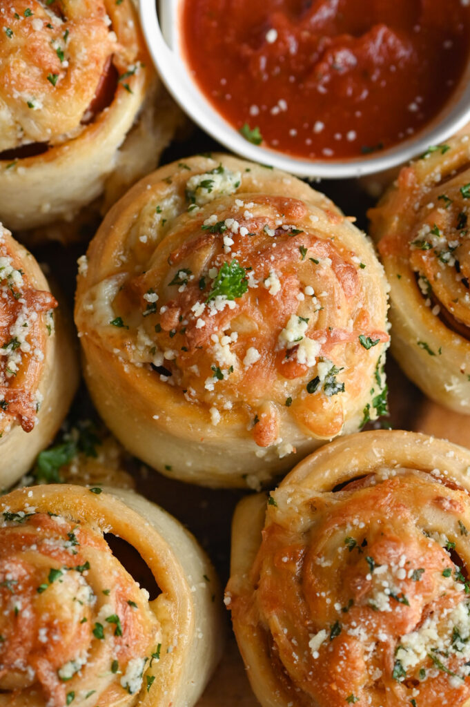 Overhead view of several rolls with cheese and parsley on top with a bowl of pizza sauce next to them.