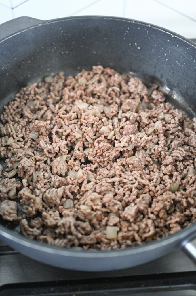 Ground beef and onions being cooked in a skillet.