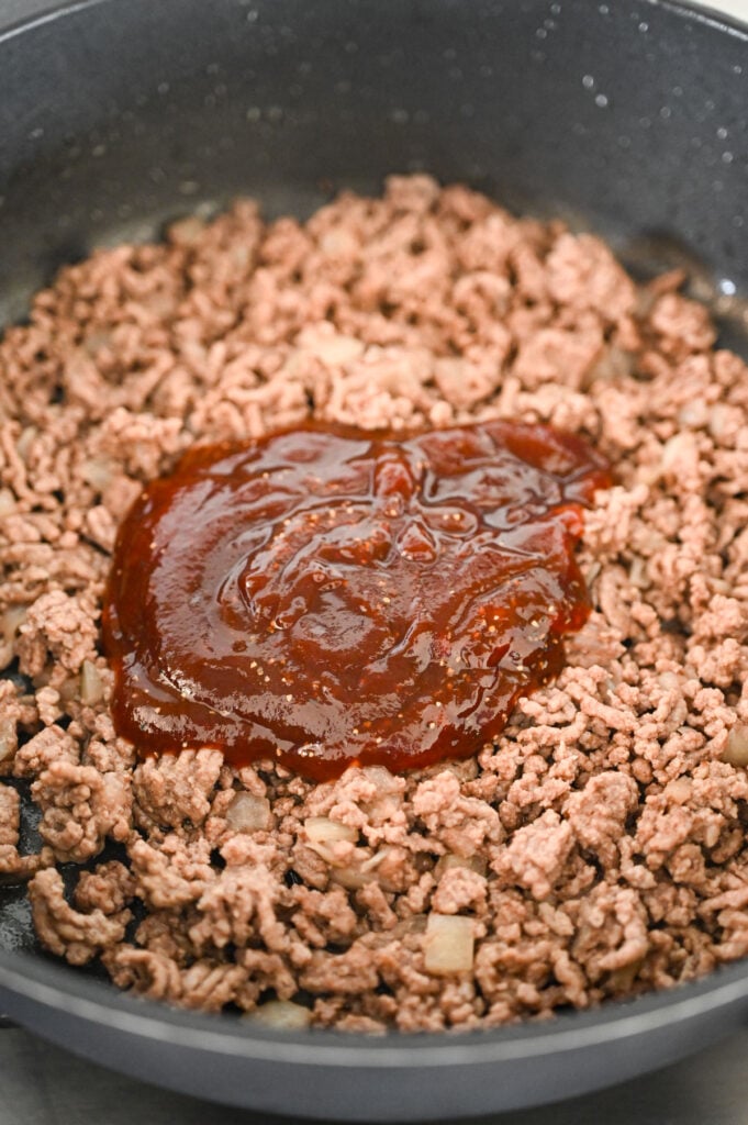 A skillet with cooked ground beef and a puddle of barbecue sauce in the middle.