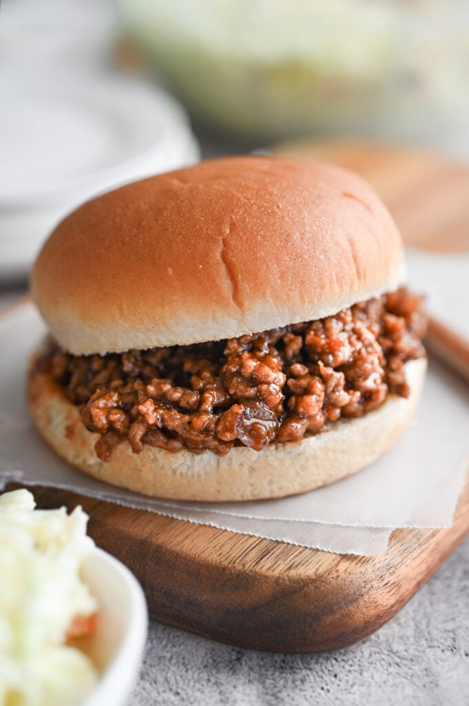 A BBQ Sloppy Joe on a wooden cutting board with coleslaw next to it.