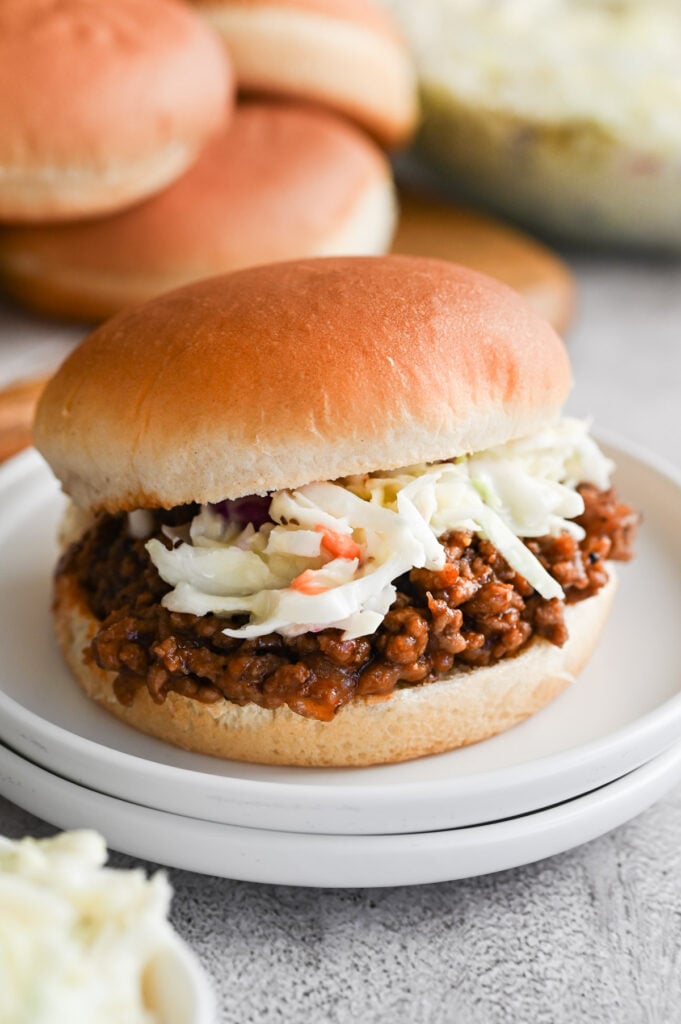 BBQ sloppy joes with coleslaw on top on a white plate.