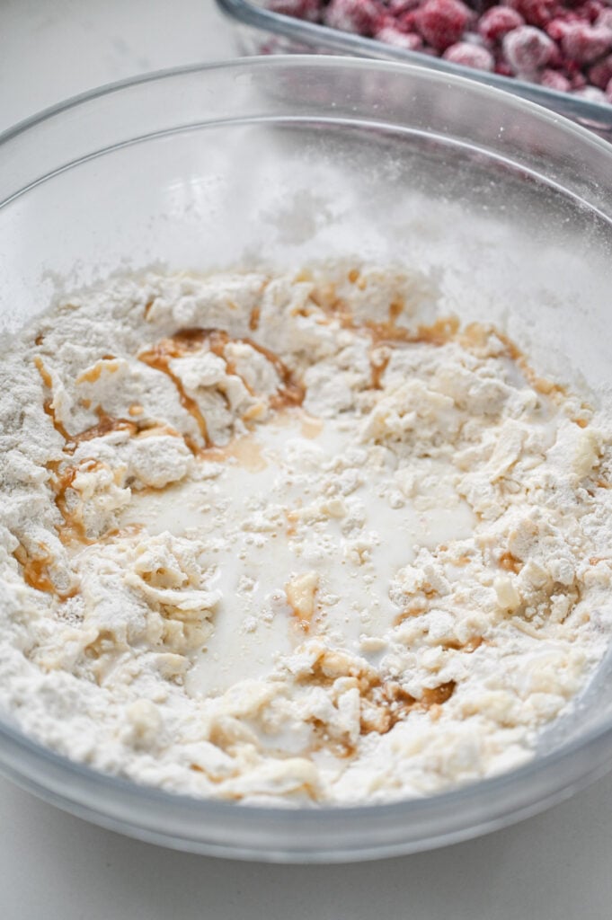 Milk and vanilla being added to a bowl of dry ingredients.