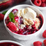 A bowl of raspberry cobbler with a scoop of vanilla ice cream on top.