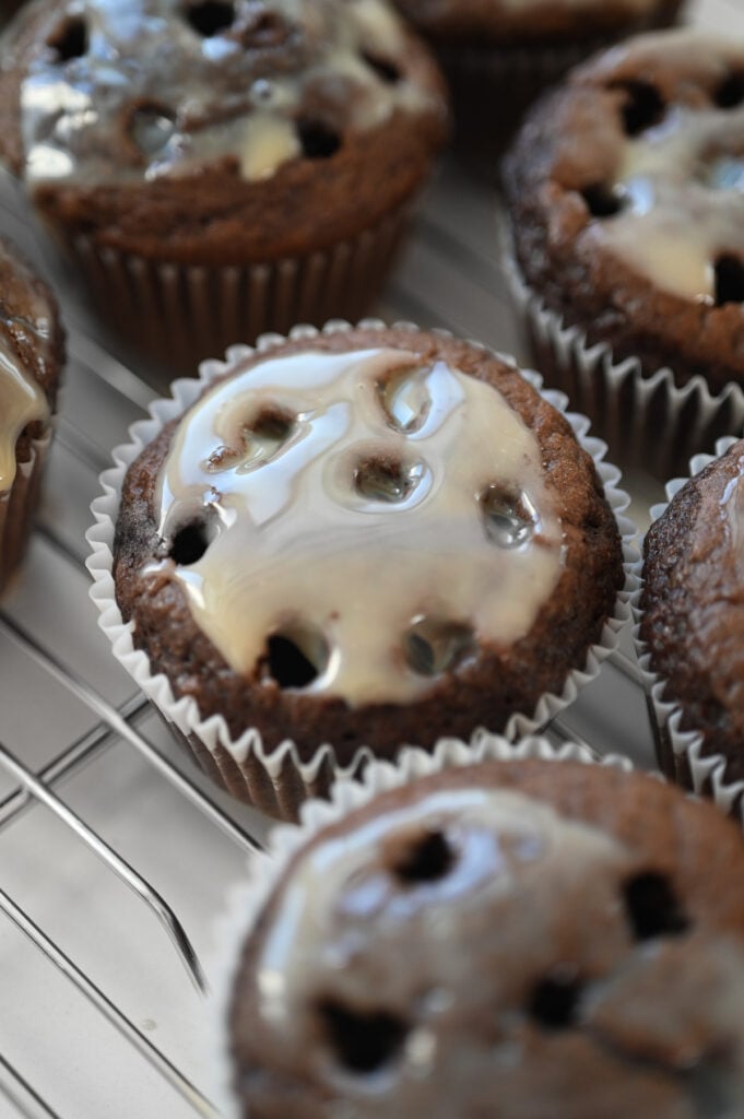 A chocolate cupcake with a shiny filling spread on top on a wire rack.