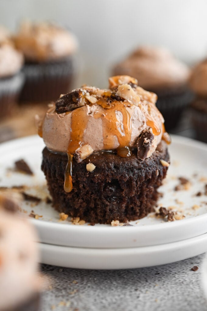 A "better than anything" cupcake after the wrapper is removed on a white plate with a drip of caramel sauce falling down the side.