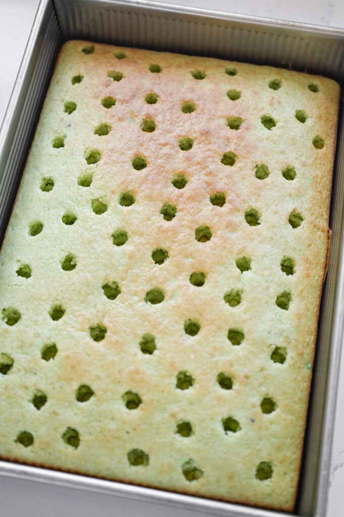 A light green pistachio cake with lots of holes (pokes) into it.