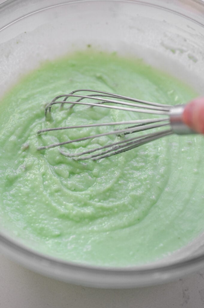 A whisk combining pistachio pudding mix and milk.