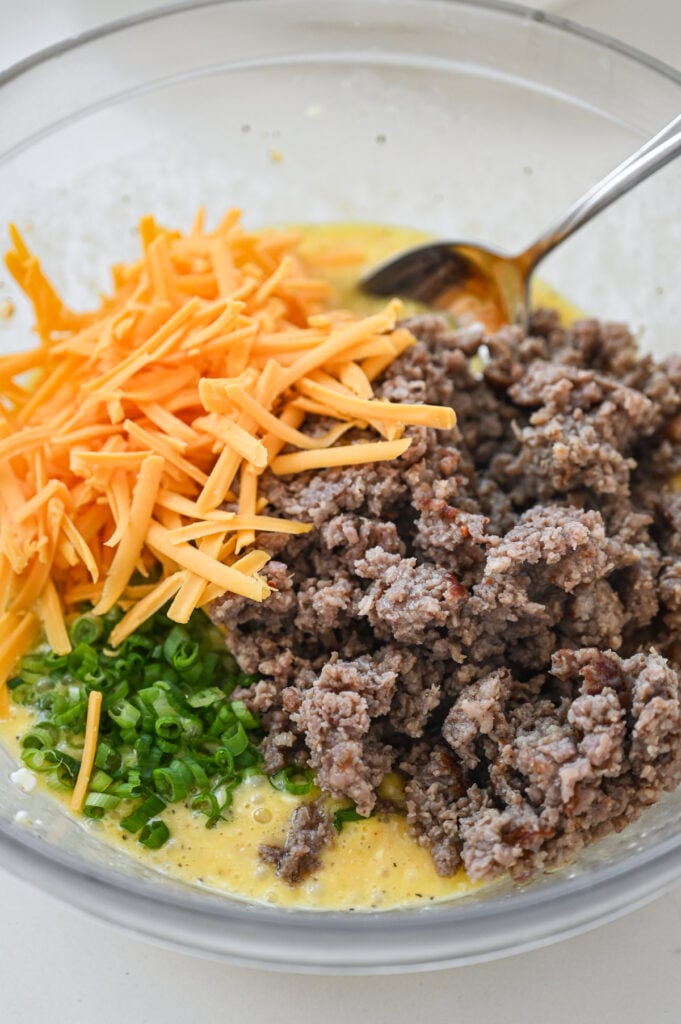 A bowl with eggs, ground sausage, green onions and cheddar cheese.