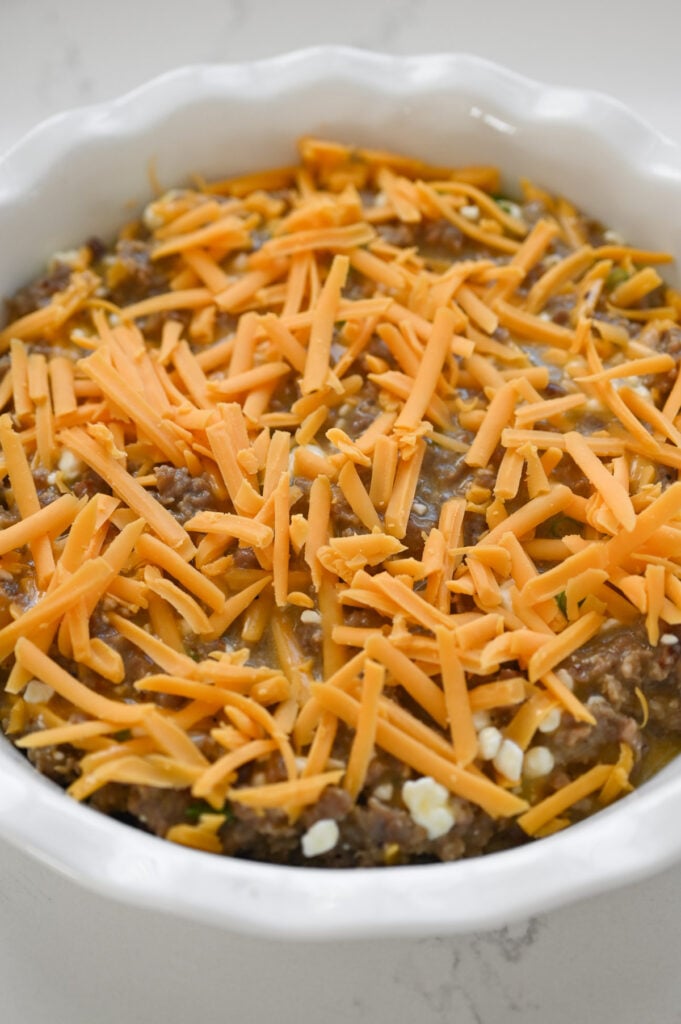 Breakfast tater tot casserole filling in a white dish with cheddar cheese on top.