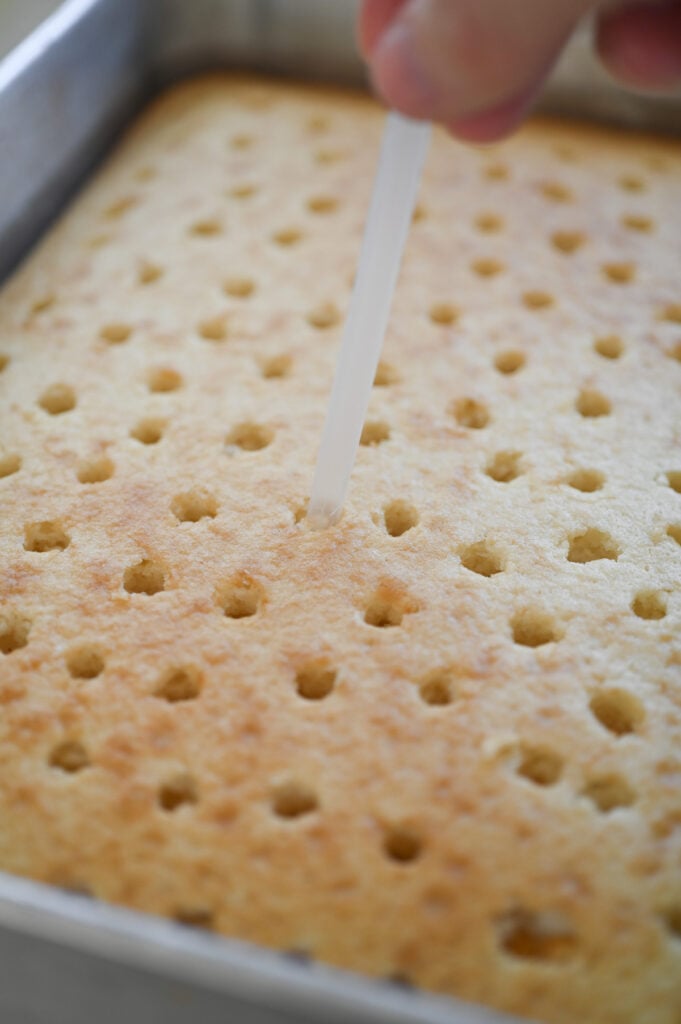 A straw poking holes into a white cake.
