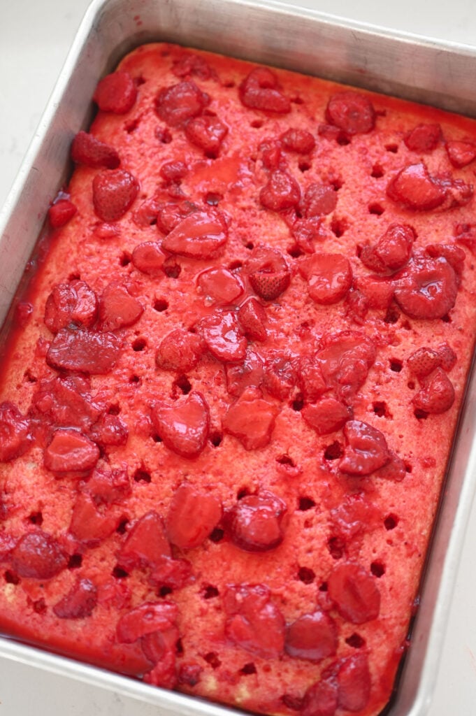 A poke cake topped with strawberry gelatin and real sliced strawberries.