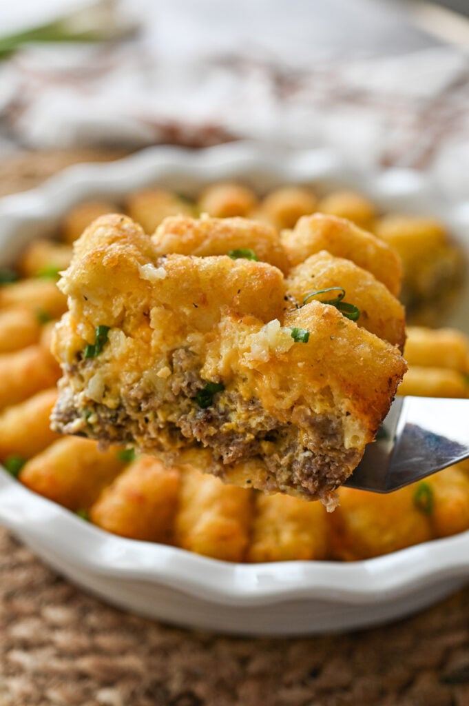 A slice of breakfast tater tot casserole being taken from a pie plate.